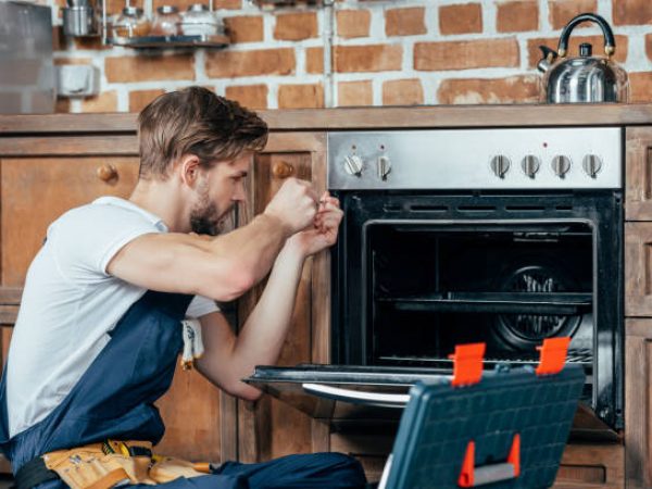 young repairman in protective workwear fixing oven in kitchen
